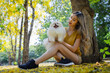 © kamonrat - Young Woman Enjoying a Peaceful Moment with Her Pomeranian on a Sunny Autumn Day in the Park, Surrounded by Nature's Beauty