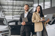 © anatoliycherkas - Super sales team in dealership, two consultants or managers in elegant suits with laptop and tablet in arms in car dealership