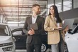 © anatoliycherkas - Super sales team in dealership, two consultants or managers in elegant suits with laptop and tablet in arms in car dealership