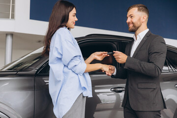 Wall Mural - Smiling salesman or manager giving car keys and shakes hand to modern happy woman new car owner in car dealership