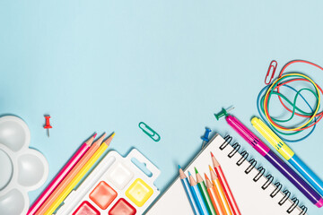 Wall Mural - Back to school concept mockup. Colorful school supplies, notepad with iron spring, paints, felt-tip pens and pencils on a blue background.