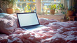 © Agustin - Laptop with blank screen on pink blanket on bed with window and plants in background