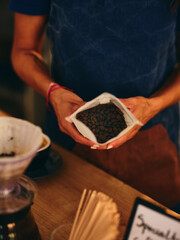 A barista wearing a dark apron carefully pours high-quality coffee beans into a filter, preparing for a fresh brew, highlighting the artisanal coffee-making process.