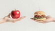 © Wimon - Side-by-side view of one hand holding a shiny apple and the other hand clutching a delicious hamburger, representing a choice between healthy and comfort food options