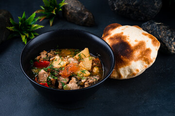 Canvas Print - Stewed pork with potatoes, sweet peppers, tomatoes, onions in tomato sauce with herbs and flatbread in a bowl.