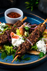 Wall Mural - Dinner kebab, barbecued beef on a stick with tomatoes, lettuce, onion, arugula, sour cream, tortilla and red sauce.