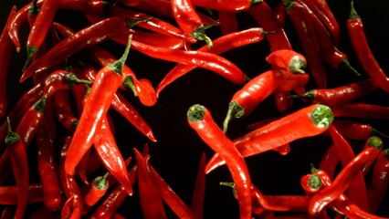 Poster - hot red chilli peppers flying on black background.