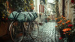 © Sawyer0 - Stary rower z dużymi torbami campingowymi stojący w malowniczej, deszczowej uliczce wyłożonej kostką brukową, wśród kwitnących roślin i rustykalnych budynków.