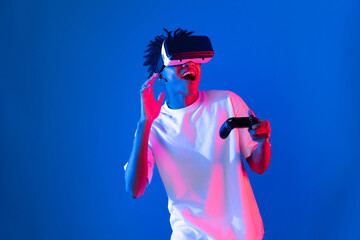 American African gaming player wearing VR controlling joystick hologram isolated blue pink neon lighting wall screen connect digital futuristic technology virtual reality metaverse world. Contrivance.