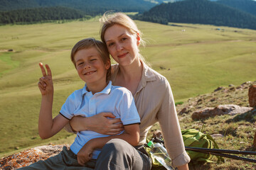 Wall Mural - Happy young woman with her son tourists resting on hill on summer day