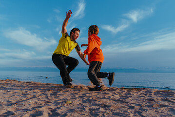 Canvas Print - Father and son playing tag on lake shore on summer day at sunset