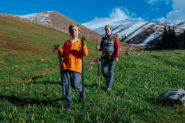 Wall Mural - Young woman tourist with her son walks in picturesque mountain valley on summer day