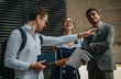 © qunica.com - Three young professionals outside discussing business strategies, analyzing reports, and planning marketing approaches for growth. Emphasizes teamwork, communication, and collaborative effort for