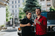 © qunica.com - Two young professionals having an animated discussion outside, standing near a car in an urban environment. The scene depicts teamwork, productivity, and collaboration.