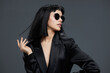© SHOTPRIME STUDIO - Woman, black suit, sunglasses a confident woman in a sleek black suit and stylish sunglasses poses with her hands on her hips and head tilted to the side against a neutral gray background