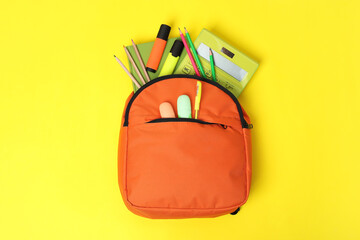 Wall Mural - Orange backpack and different school supplies on yellow background, top view