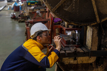 Male mechanical or metallic engineer is using a torch light to check a welding machine for maintenance and quality control. Expert is inspecting or repairing an automatic machine in a metallic factory