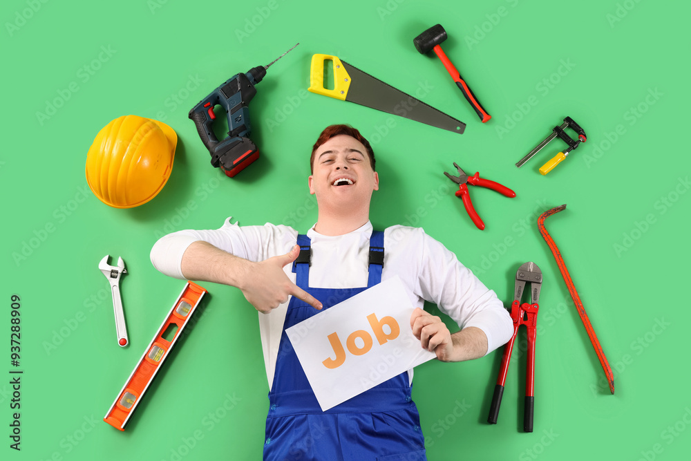 Male builder pointing at paper with word JOB and work tools on green background, top view