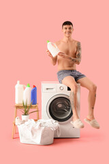 Wall Mural - Young man in underpants with detergent sitting on washing machine against pink background