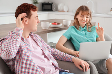 Canvas Print - Young man with hearing aid and his girlfriend using laptop in kitchen