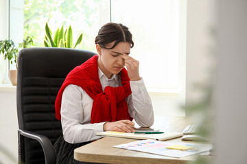 Young woman suffering from headache at workplace with notebook in office