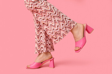 Canvas Print - Legs of young woman in trousers and pink open-toed high heels on pink background