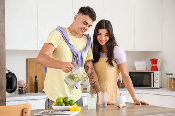 Canvas Print - Happy young couple pouring fresh mojito into glasses in kitchen