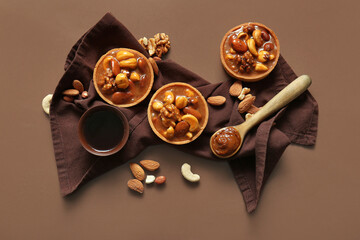 Wall Mural - Tasty tarts with nuts and caramel sauce on brown background