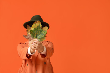 Poster - Beautiful young happy African-American woman in stylish outfit with autumn leaves on orange background