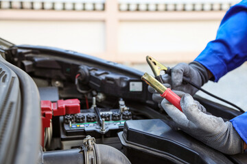 Car mechanic holding connect jumper cable or car booster cables on terminal dead battery for jump-start or check car battery fail problem change repairing and fix car with maintenance service.