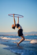 © Cavan Images - Woman hula hooping near the shore during sunset at the beach