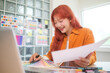 © wattana - Smiling female graphic designer  selecting colors for her project at desk.