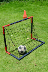 Soccer ball in goal net on green grass field with red cones