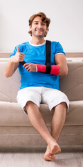 Wall Mural - Young man with injured arm sitting on the sofa