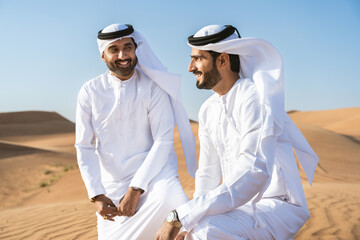 Wall Mural - Two middle-eastern emirati men wearing arab kandura bonding in the desert