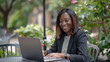 © liliyabatyrova - A woman with a radiant smile sits outside at a garden table, focused on her laptop. The lush greenery around her enhances the atmosphere of creativity and joy