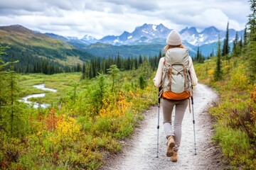 A person hiking on a scenic trail surrounded by lush greenery and majestic mountains under a cloudy sky.