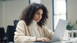 © halo - A portrait of an attractive Hispanic woman with curly hair, sitting at a desk, and typing on a laptop computer.