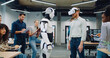 © ihorvsn - Multi-ethnic teach of engineers and programmers surrounding their new creation. Male with VR headset moving and operating humanoid robot. Checking synergy. Testing. People happy about success.