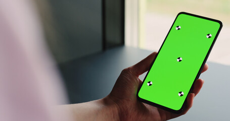 Sticker - young woman sitting at the black table near window and holding smartphone with vertical green screen