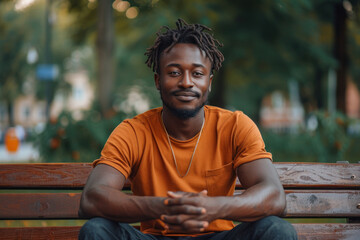 Wall Mural - Confident young man with dreadlocks sitting on park bench smiling