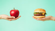 © StellaPattaya - One hand holding apple fruit, other holding hamburger. Healthy natural organic fresh vegetarian food vs unhealthy processed fast junk food meat. Nutrition diet lifestyle, fitness eating choice