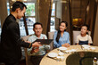 © DragonImages - Waiter giving menu to family to make order in the restaurant