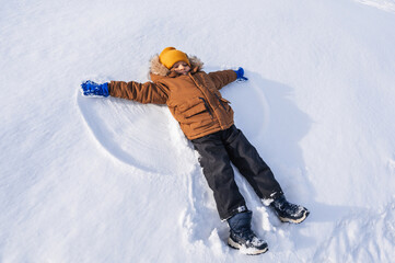 Wall Mural - A five-year-old Caucasian boy lies in the snow and makes a snow angel