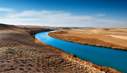 Wall Mural - A river with a blue color runs through a dry, brown field