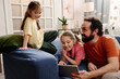 © pressmaster - Father sitting with daughters while interacting together in living room Family time creating close bond and happy moments together indoors