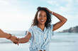 © peopleimages.com - Portrait, lead and happy woman holding hands at beach for summer travel, vacation and laugh at funny joke. Face, smile and pov of couple to sea for holiday, relax or follow partner for love on island