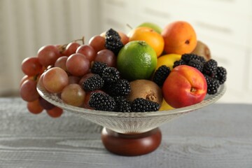 Wall Mural - Glass vase with different fruits and berries on grey wooden table indoors, closeup