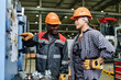 © pressmaster - Two factory workers wearing safety gear discussing operation of machine in manufacturing facility with industrial equipment in background