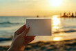 © VaCity - Hand Holding Blank Card at Beach Sunset